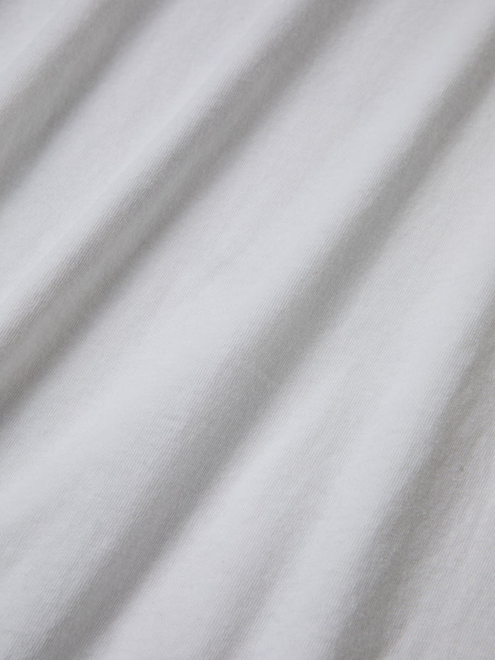 Close-up of white 100% cotton fabric with visible texture and subtle shadowing from folds, reminiscent of the classic Malibu Farm Fair Tee by FOUND.