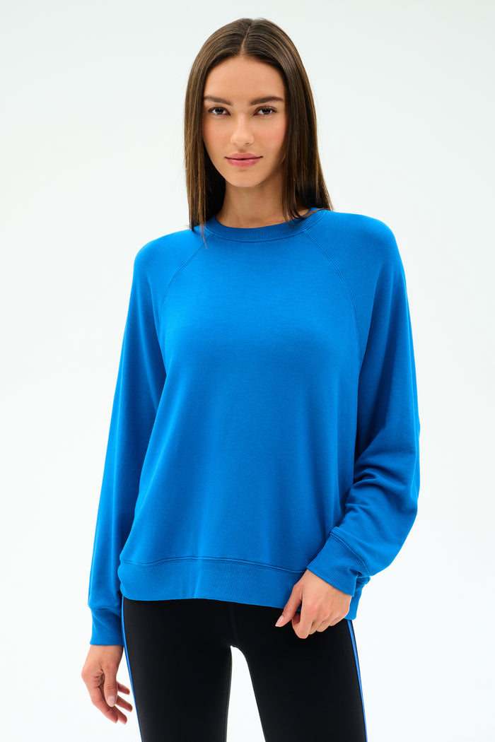 A woman wears the SPLITS59 Andie Oversize Fleece Sweatshirt in Classic Blue with black leggings, standing against a plain light background.