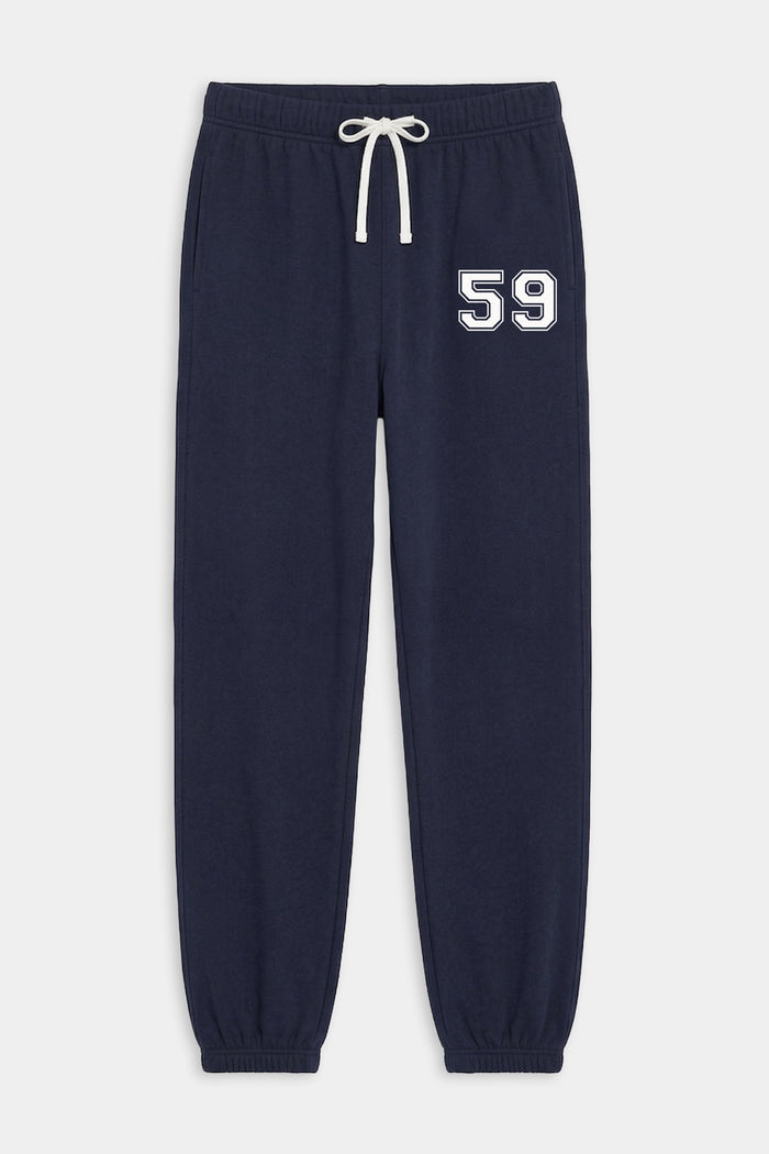 The SPLITS59 Andie Oversized Fleece Varsity 59 Sweatpant in Indigo features elastic cuffs, a white drawstring, side pockets, and "59" on the left thigh. Made in Los Angeles.