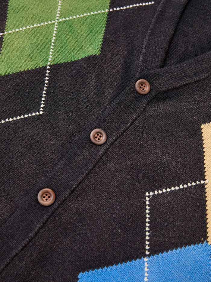 Close-up of the FOUND Argyle Knit Cardigan, an oversized black knit with brown buttons and a vibrant green, yellow, and blue argyle pattern.