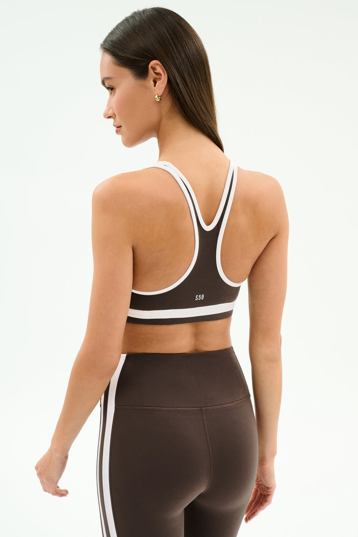 A woman models the SPLITS59 Bianca Rigor Bra in Dark Chocolate/White, paired with matching high-waisted leggings, seen from the back against a light backdrop—perfect for high-impact workouts or intense gym sessions.