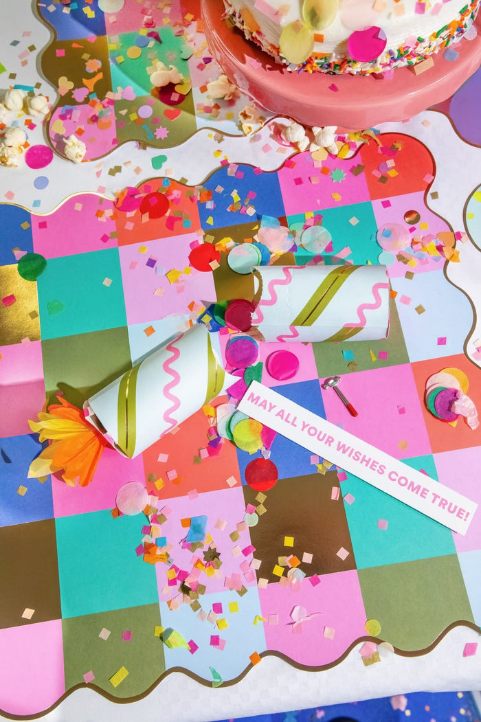 Colorful birthday card with confetti, a party horn, and a small cake on a checkered background.