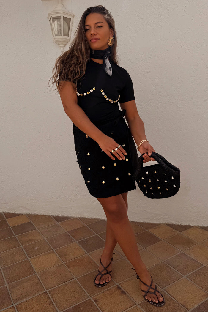 Black Crochet Shell Wrap Skirt with gold shell details and a tie waist, styled with strappy sandals.