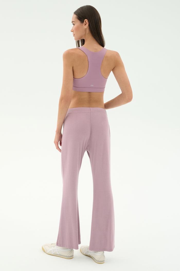 A woman faces away, wearing the SPLITS59 Blaire Rib Pant in blush with a matching lavender sports bra and white sneakers, set against a plain, light background. The outfit is crafted from soft modal fabric with added spandex for comfort.