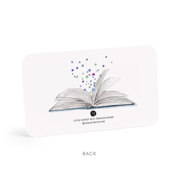 The back of a white card or packaging insert featuring an illustration of an open book with colorful stars rising from it. Text on the card reads 'LITTLE NOTES BY E.