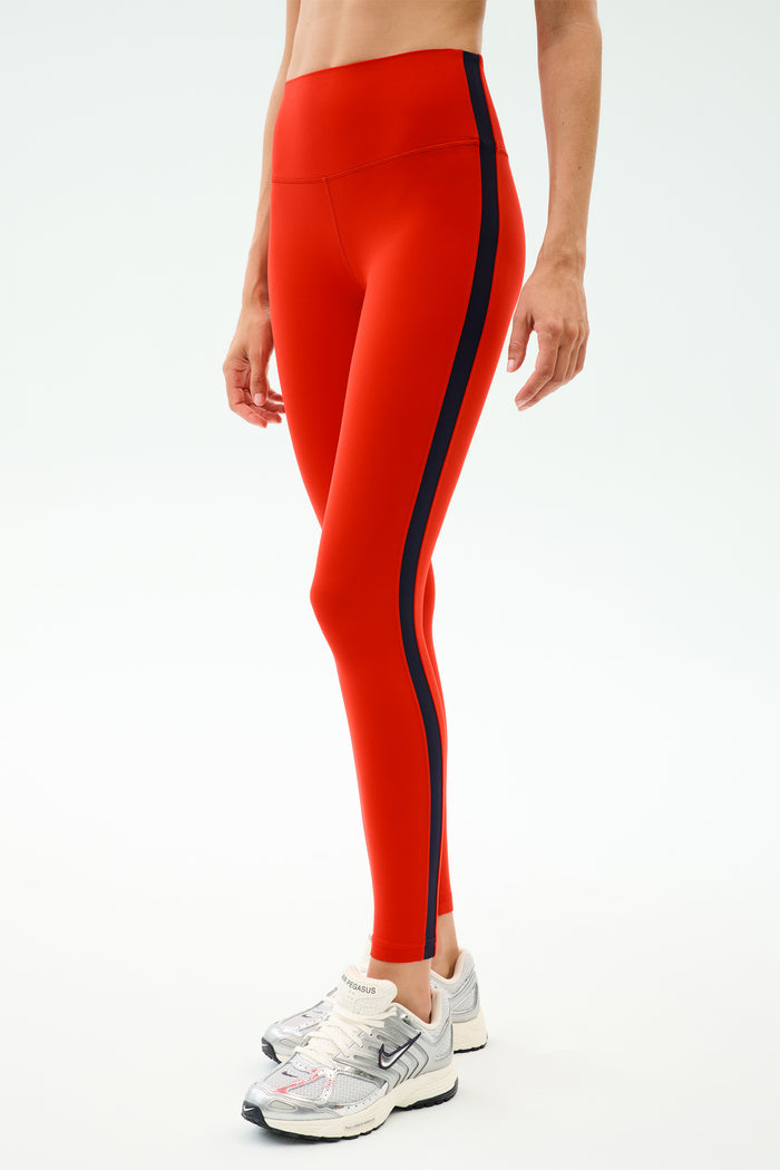 Person wearing SPLITS59 Clare High Waist Rigor 7/8 leggings in Lotus Red/Indigo, featuring a striking high waist and indigo side stripe—ideal for gym workouts or making a stylish statement.