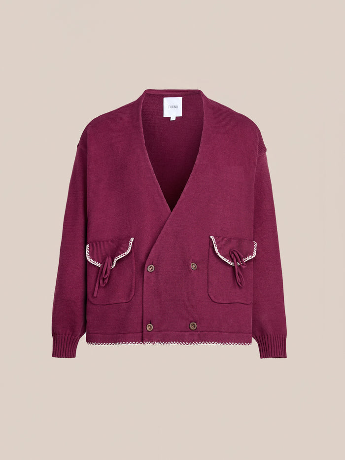 The FOUND Double Breasted Bow Cardigan is a maroon unisex knit with a relaxed fit, two front pockets, button closures, and decorative trim on the pockets and hem, shown against a plain background.