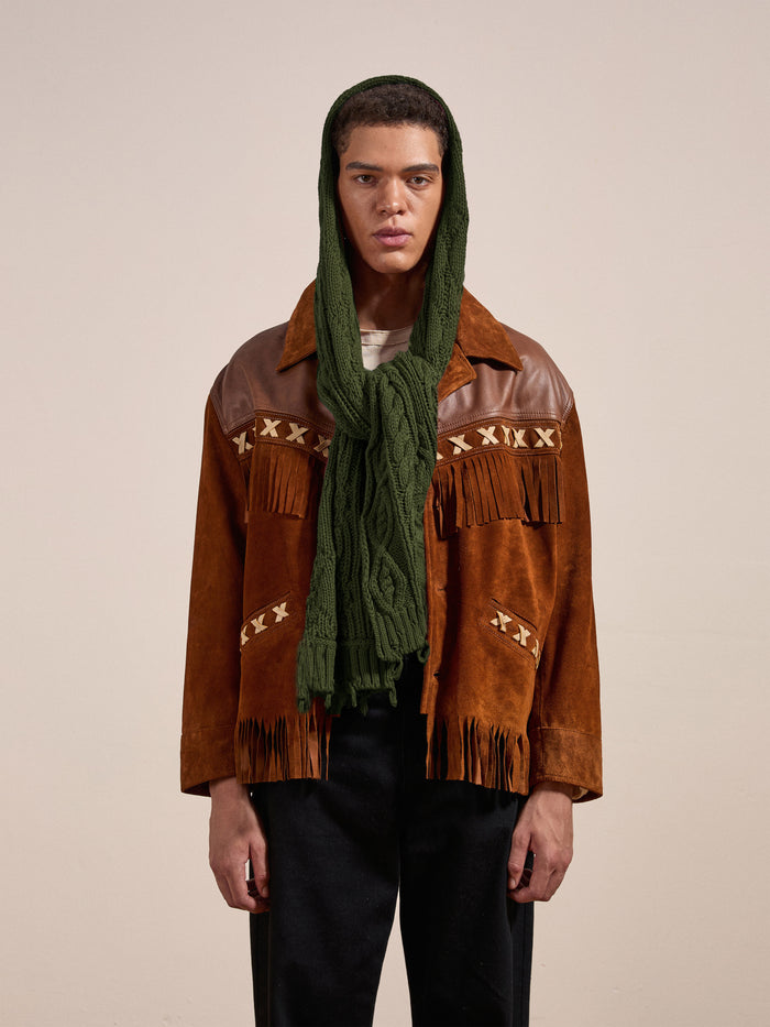 A person wearing a brown suede jacket with fringe details and a Forest Distressed Cable Knit Scarf from FOUND over their head stands against a plain backdrop.