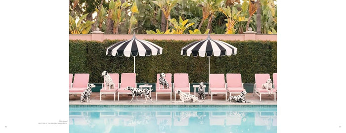 A square art print featuring a luxurious poolside scene with pink lounge chairs, two black and white striped umbrellas, and Dalmatian dogs lounging by the water, set against a green hedge and tropical foliage.