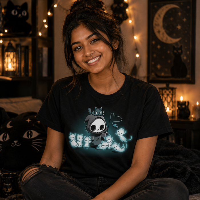 Women's Premium T-Shirt_TeeTurtle Grim and Kitties black t-shirt featuring a hooded skeleton figure, resembling a spooky Grim Reaper, standing surrounded by glowing ghostly cats. One cat is perched on its head while it playfully dangles a toy fish in front of the others.