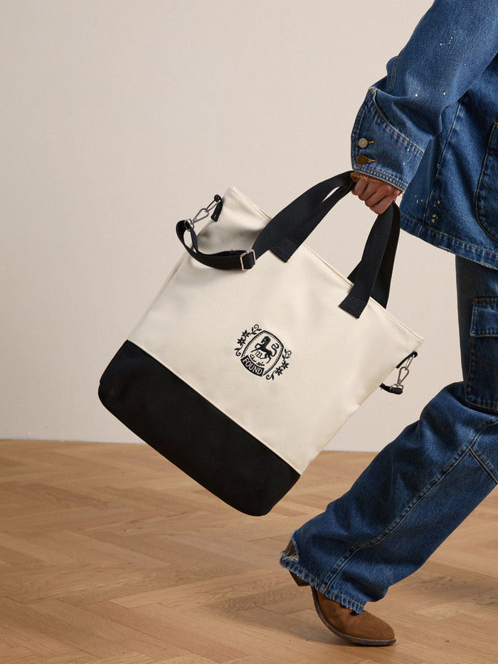 A man is carrying a white and black Profound Horse Logo Crest Canvas Bag.
