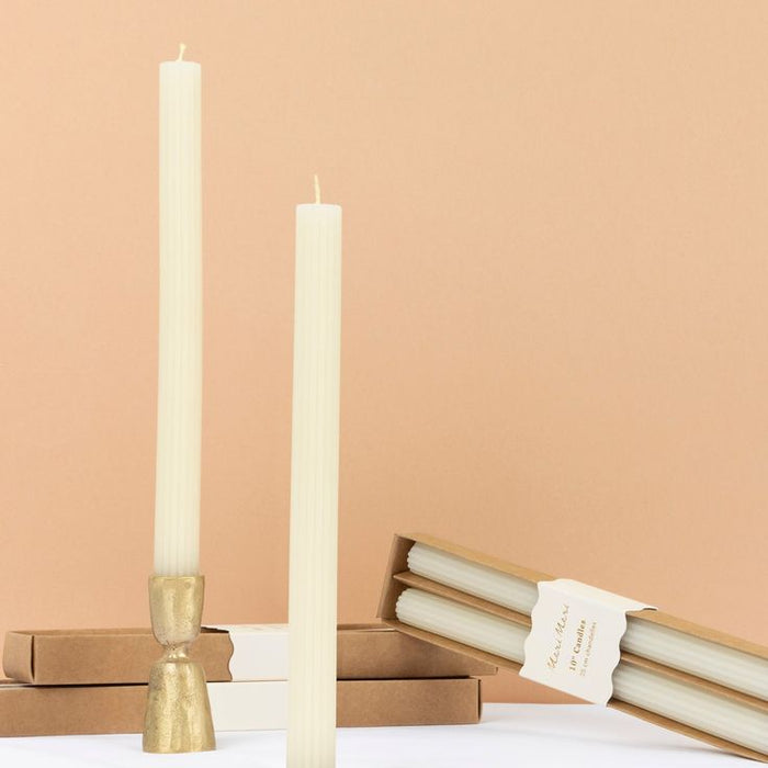 Two tall white candles with gold holders on a beige background