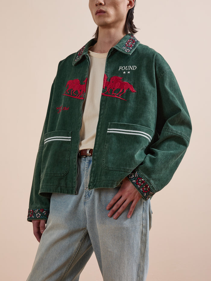 A person wears a Found Jockey Club Embroidered Jacket with racing horses, patterned collar and cuffs, a beige shirt, and light blue unisex relaxed fit jeans.