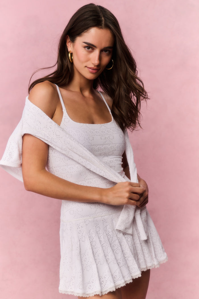 Woman wearing a white lace sleeveless mini dress against a pink background