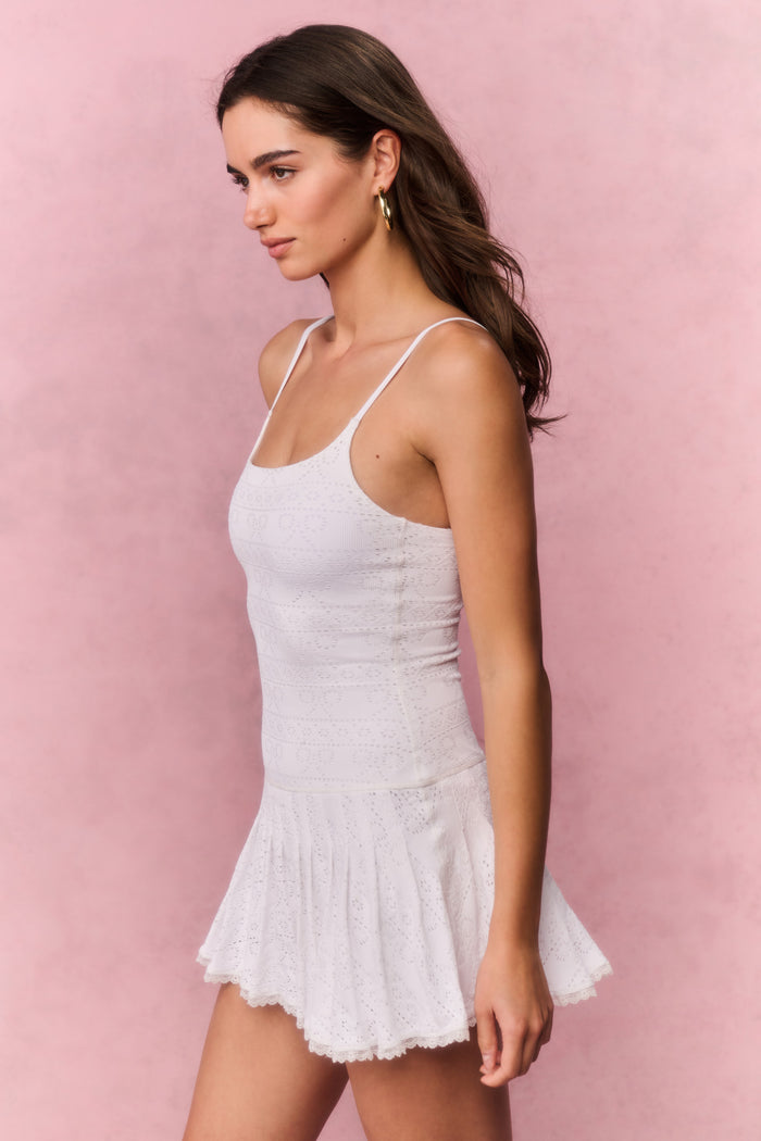 Woman wearing a white lace sleeveless mini dress against a pink background