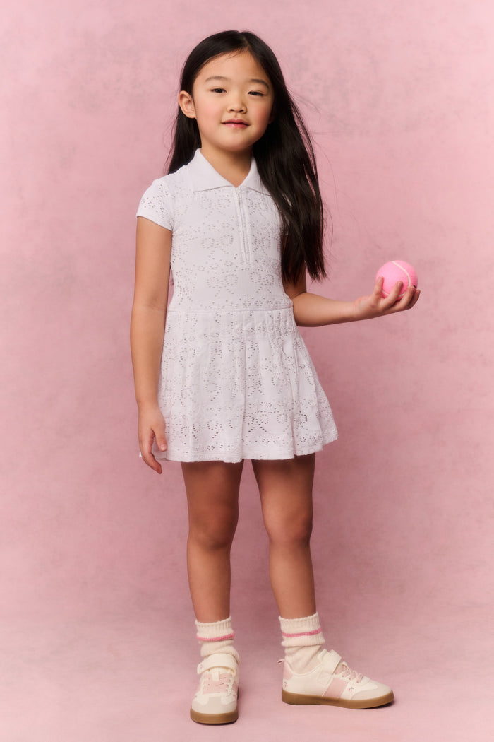 Young girl wearing a white t-shirt dress against a pink background