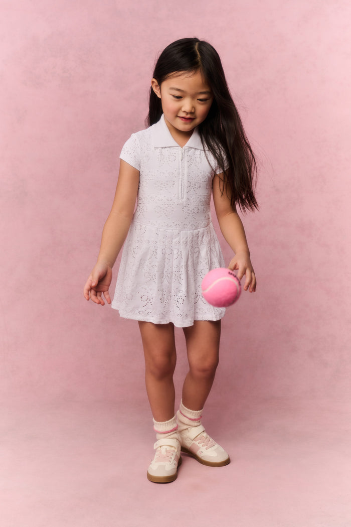 Young girl wearing a white t-shirt dress against a pink background
