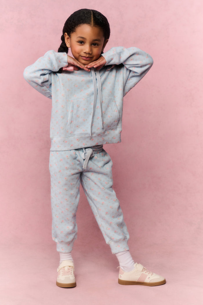 Young girl wearing a light blue tracksuit against a pink background