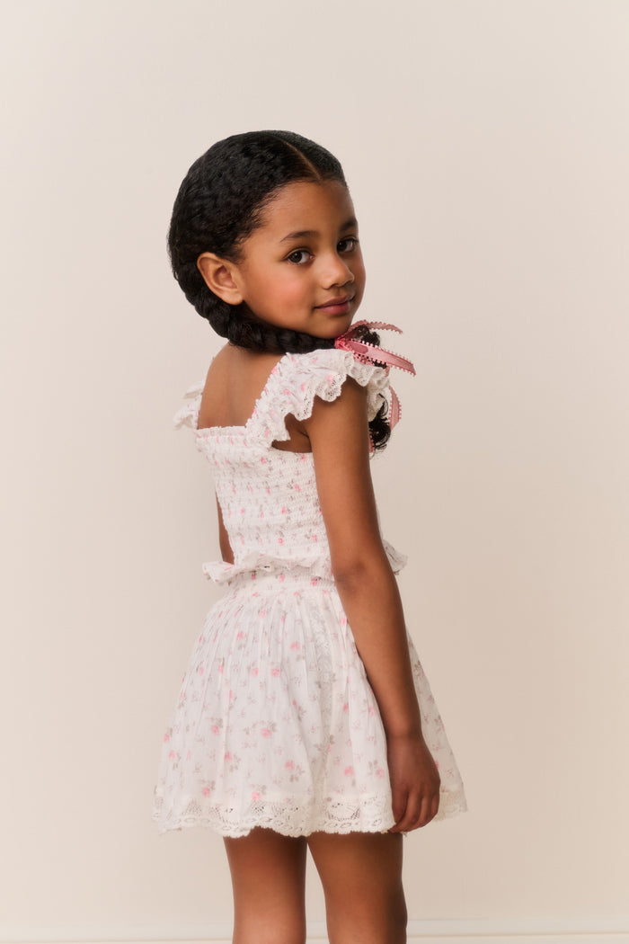 Young girl wearing a Light pink lace floral skirt and top with pink floral patterns on a plain background