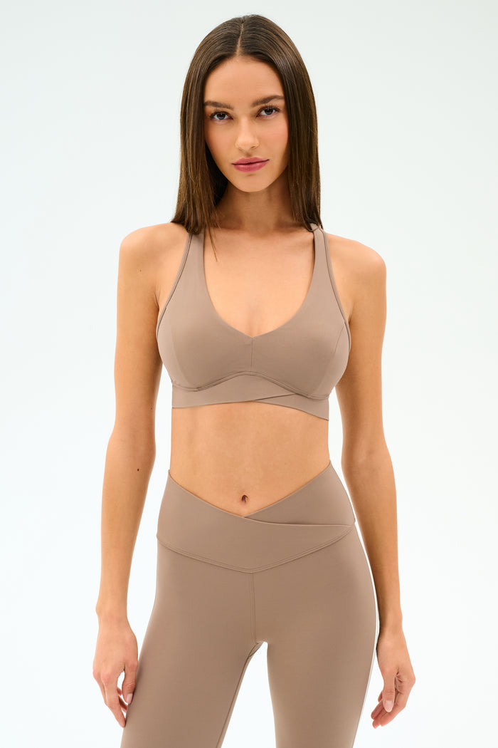 A woman faces forward in a taupe SPLITS59 Mia Rigor Bra - Latte and matching high-waisted leggings, set against a plain light background.