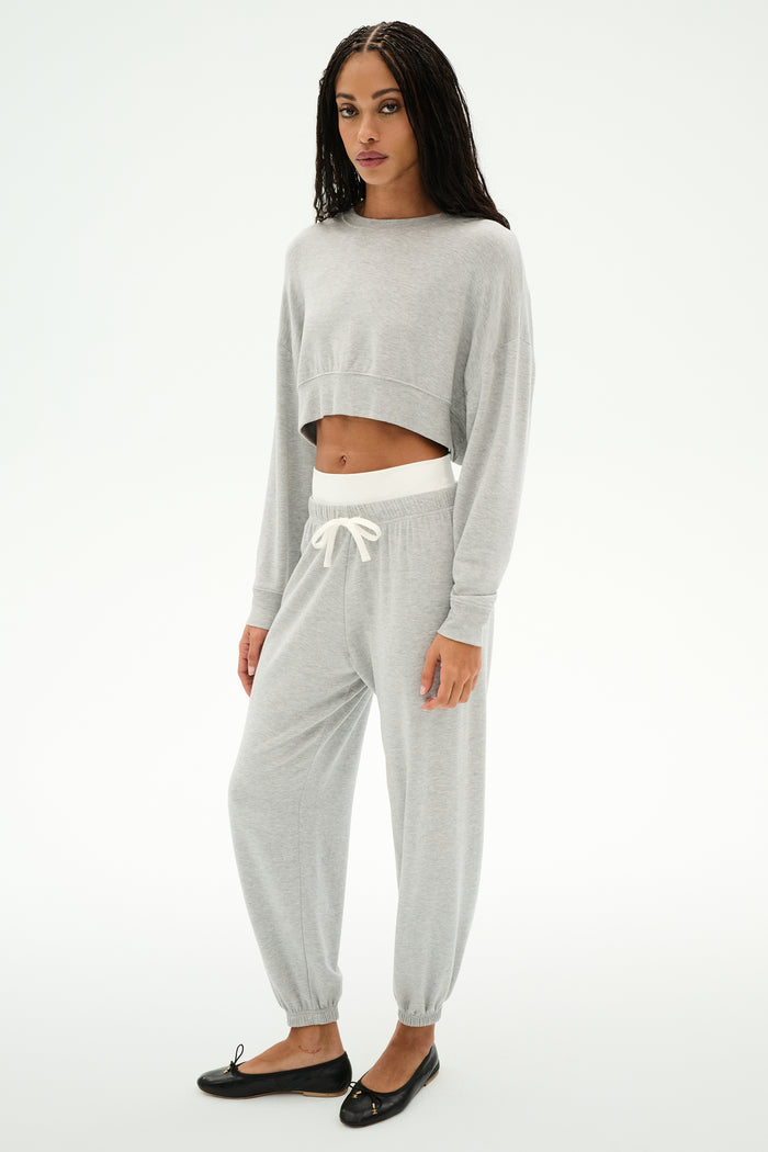 A woman wears the SPLITS59 Noah Fleece Crop Sweatshirt in Heather Grey with matching sweatpants and black flats, standing against a plain white background.