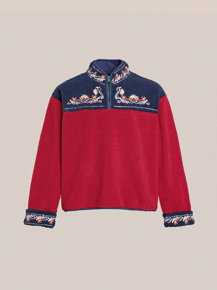 The FOUND Pahari Floral Embroidered Sherpa Pullover is a long-sleeve fleece garment with a red body and navy blue yoke, showcasing intricate Pahari style embroidery on the chest and cuffs.