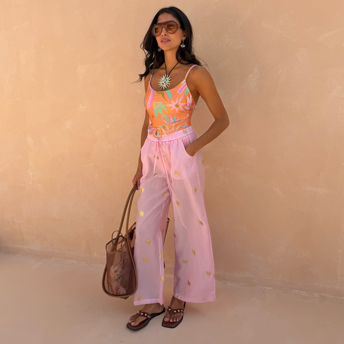 Pink Elissa Trousers featuring gold foil sun motifs, a wide-leg fit and elasticated waist, styled for a vacation look.