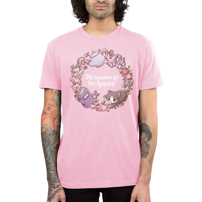 Premium Cotton T-shirt_TeeTurtle light pink Reasons to be Happy apparel featuring the caption, “Reasons to be Happy“ surrounded by a wreath with a cat, tea, flowers, books, butterflies, and strawberries.