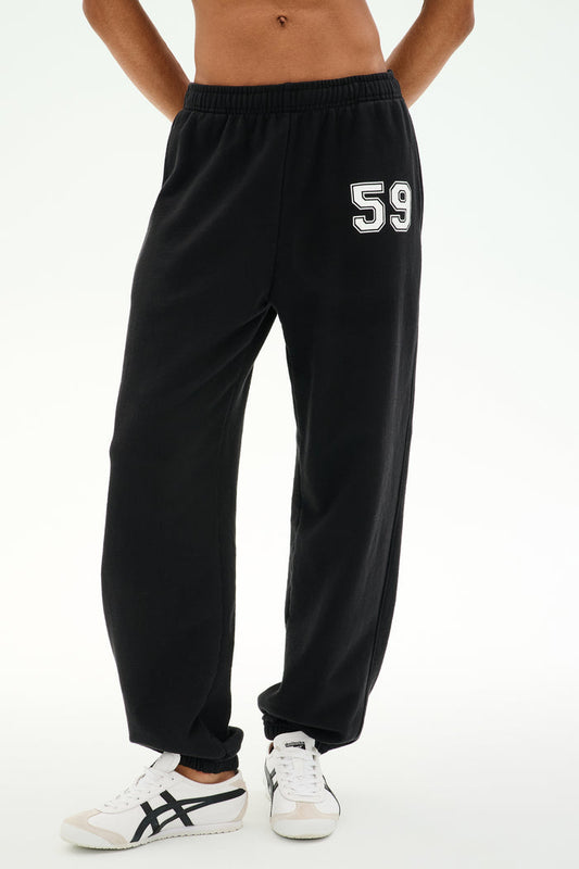A person is wearing the SPLITS59 Serena French Terry Oversized Sweatpant in black with a “59” on the left thigh, paired with white sneakers featuring black accents, standing against a plain background; these sweatpants are made in Los Angeles.