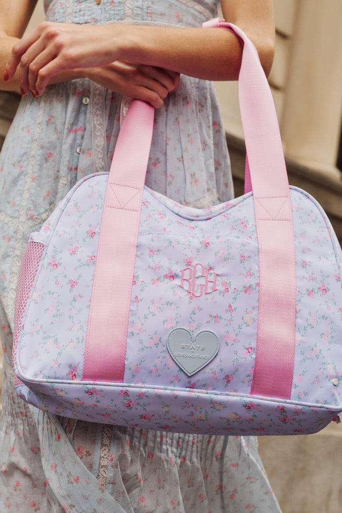 Floral-patterned bag with pink straps held by a person wearing a light dress.