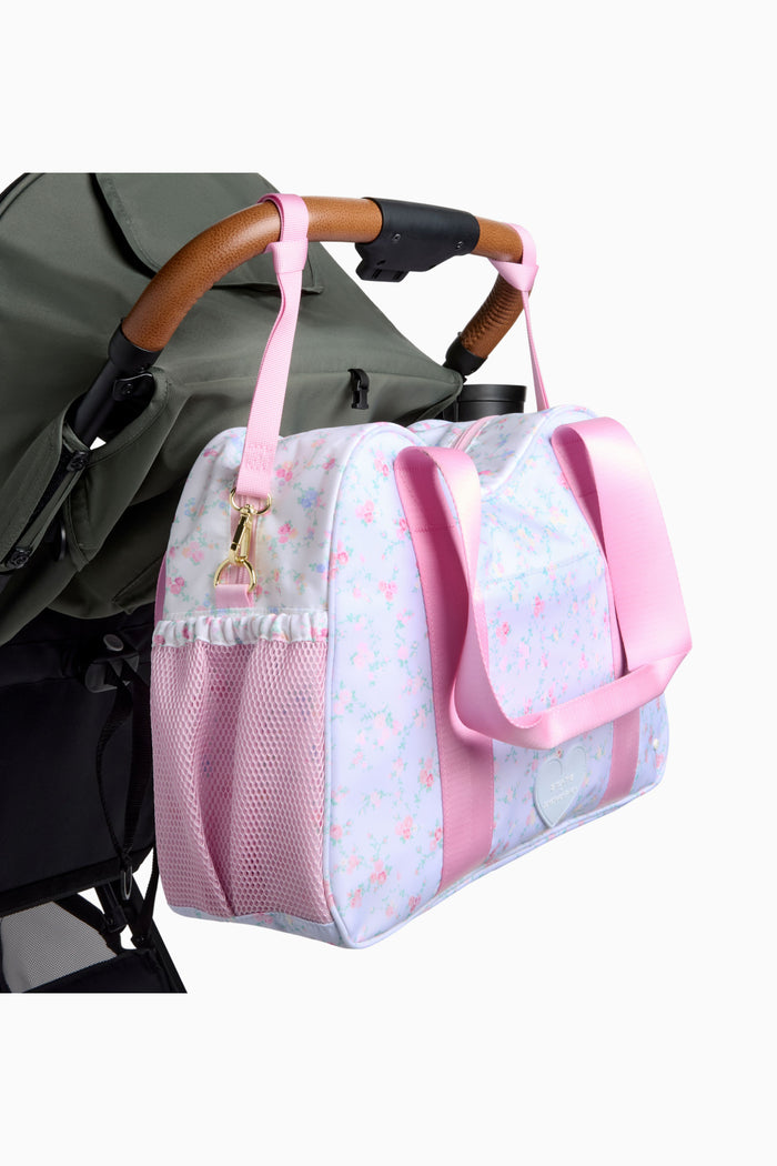 Pink and white diaper bag attached to a stroller on a white background