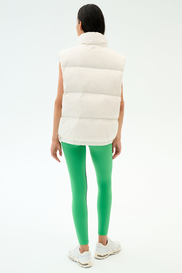 Wearing the SPLITS59 Summit Nylon Puffer Vest in white, paired with bright green leggings and white sneakers, a person stands facing away—showcasing a lightweight, stylish option for cool weather workouts against a plain background.