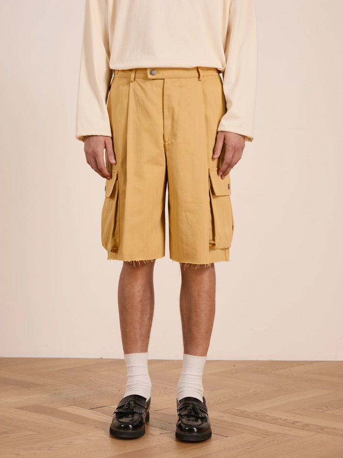 A person wearing a unisex long-sleeve beige shirt, FOUND Sunlight Twill Cargo Shorts, white socks, and black loafers stands on a wooden floor.