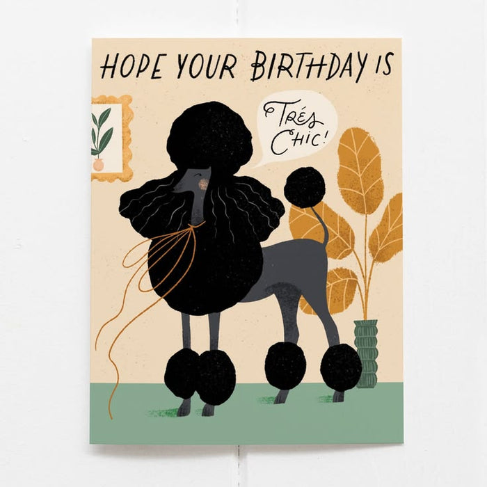 Birthday card with a stylized illustration of a person with a large afro, text 'Hope your birthday is Trés Chic', and decorative elements on a beige background.